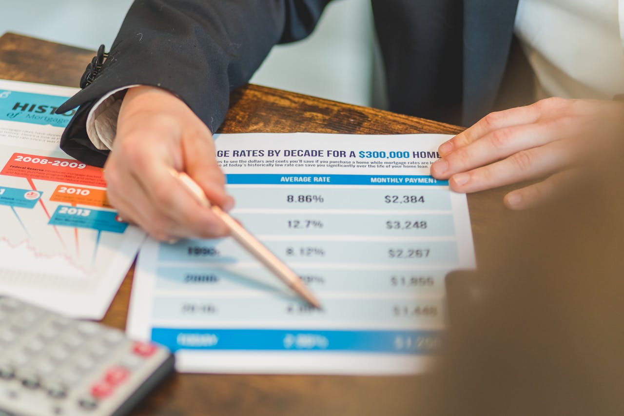 Home A close-up of hands analyzing mortgage rate documents with a pen and calculator in a business setting.